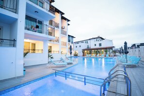 A hotel with a swimming pool, lounge chairs, and a restaurant.
