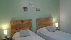 Et værelse med to senge, begge med trægavl og hvidt sengetøj. Der er vægmonterede lamper og et lille bord med en lampe.