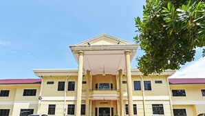 A two-story building with a central entrance, large columns, and a red-tiled roof.