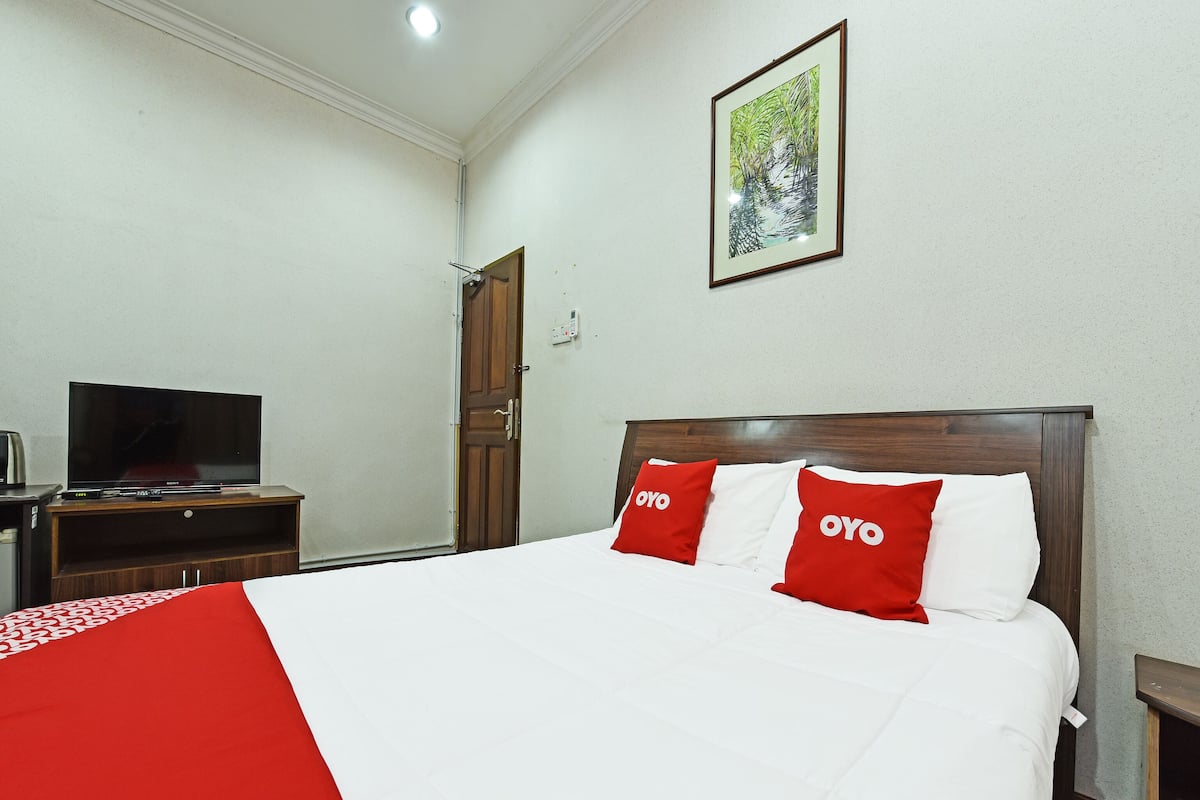 A hotel room with a bed, a TV on a stand, a door, and a framed picture on the wall.