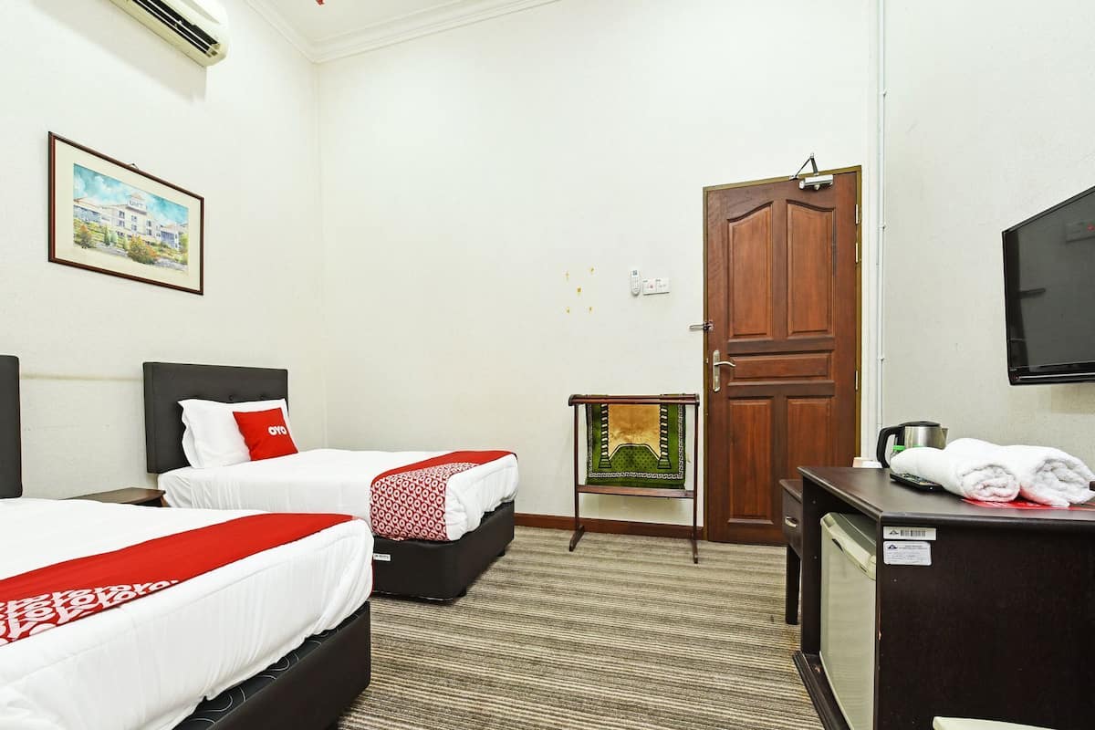 A hotel room with two beds, a desk, a television, and a door.