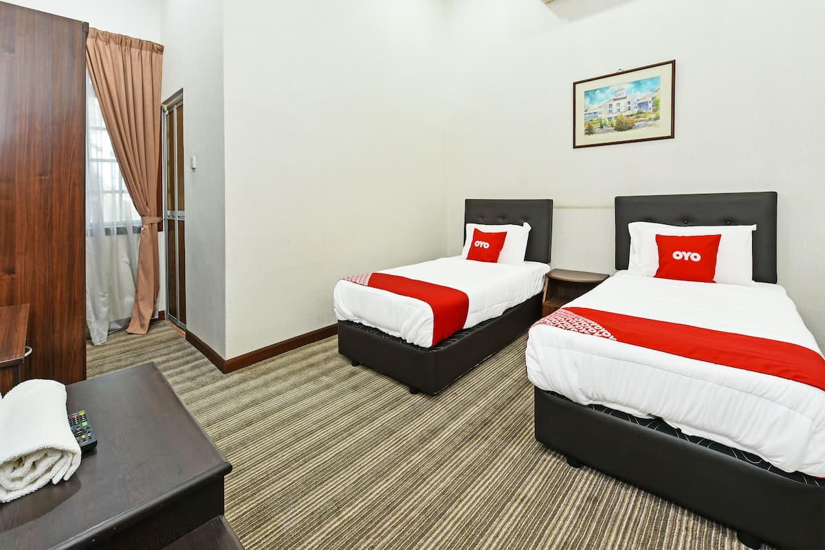 A hotel room with two beds, a wooden desk, a remote control, and a painting on the wall.