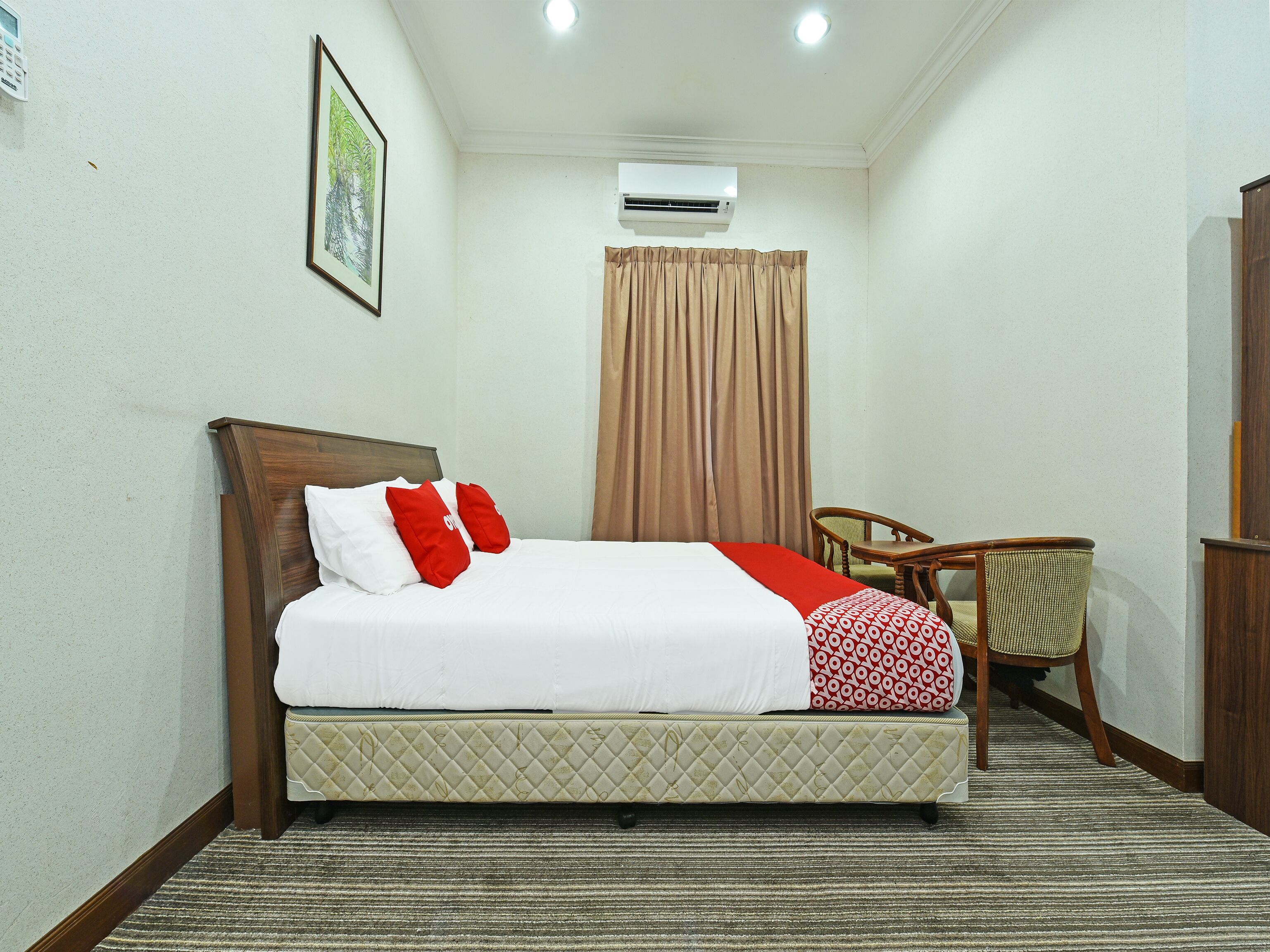 A neatly arranged hotel room with a bed, a chair, a desk, and an air conditioning unit.