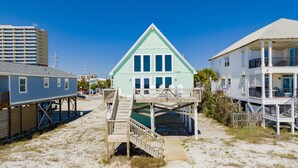 Une propriété située en bord de mer, avec un bâtiment bleu clair remarquable, doté d’un balcon et d’un escalier en bois menant à une terrasse.