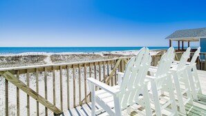 Une vue sur la plage avec une terrasse en bois et des chaises blanches.