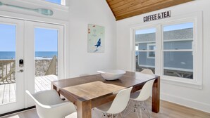 Un coin repas avec une table en bois, des chaises blanches, un bol blanc et une pancarte indiquant « CAFÉ ET THÉ ».