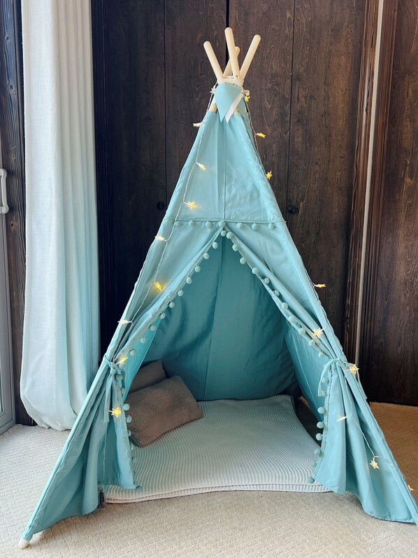 A light blue teepee with star decorations, a brown cushion, and a textured rug on the floor.