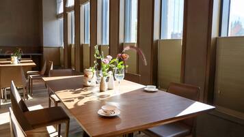 A dining area with wooden tables and chairs, a vase with flowers, and a glass of water on one table.