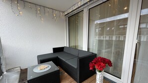 A balcony with a black sofa, a small table with a decorative item, and a white vase with red flowers. - Shopping, vacation or business - you've finally come to the right place (Metzingen)