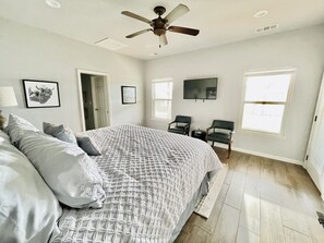 Ein Schlafzimmer mit einem großen Bett, einem Deckenventilator, zwei Stühlen, einem Fernseher und einer Tür.