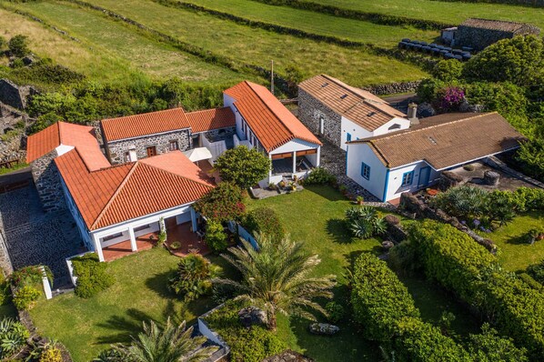 Un vaste domaine comprenant plusieurs bâtiments, dont une maison principale avec un toit recouvert de tuiles rouges et une construction plus petite dotée d’une façade en pierre.