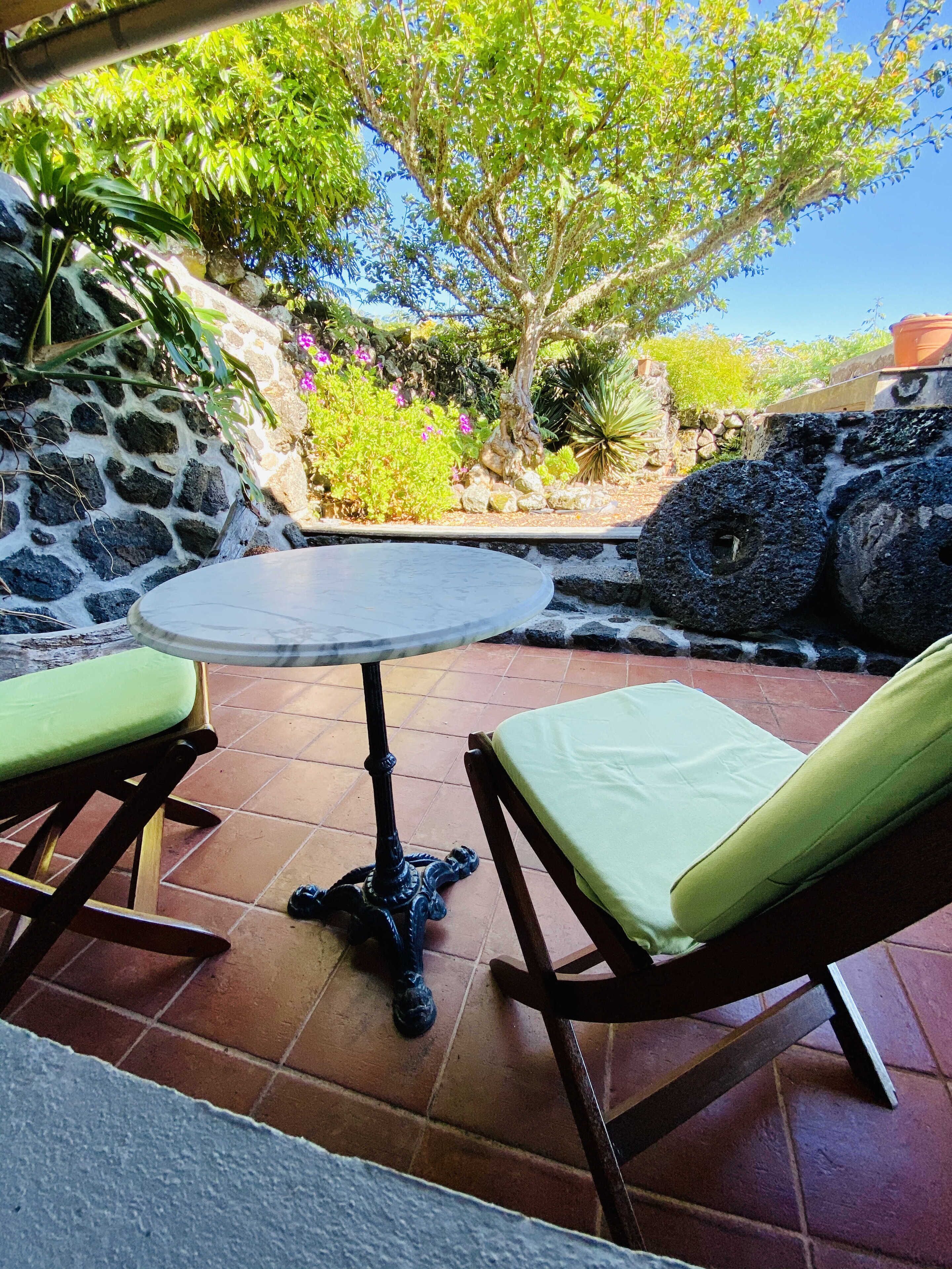 A patio with a round table and two chairs, surrounded by stone walls and greenery.