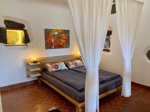 Une chambre à coucher avec un lit, un baldaquin, un tableau et une étagère sur laquelle se trouve une bougie.