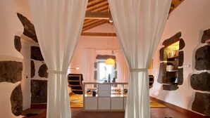 Une chambre à coucher avec un lit, des rideaux blancs, des murs en pierre, un plafond en bois et une vue sur la pièce.