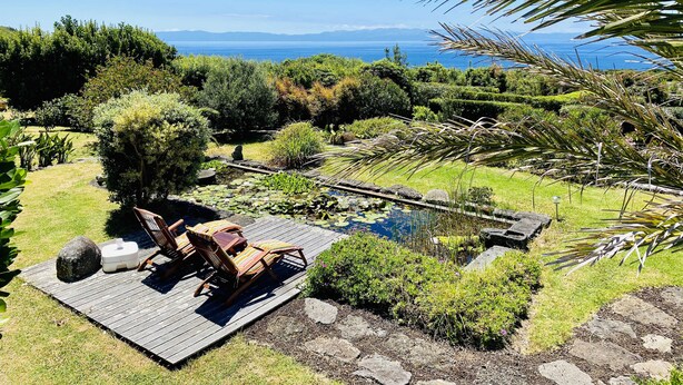 Une terrasse dotée de mobilier d’extérieur, offrant une vue sur un jardin et un plan d’eau.