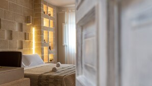 Et hotelværelse med en stenvæg, en seng med et vamset tæppe og et lille bord med en stol.