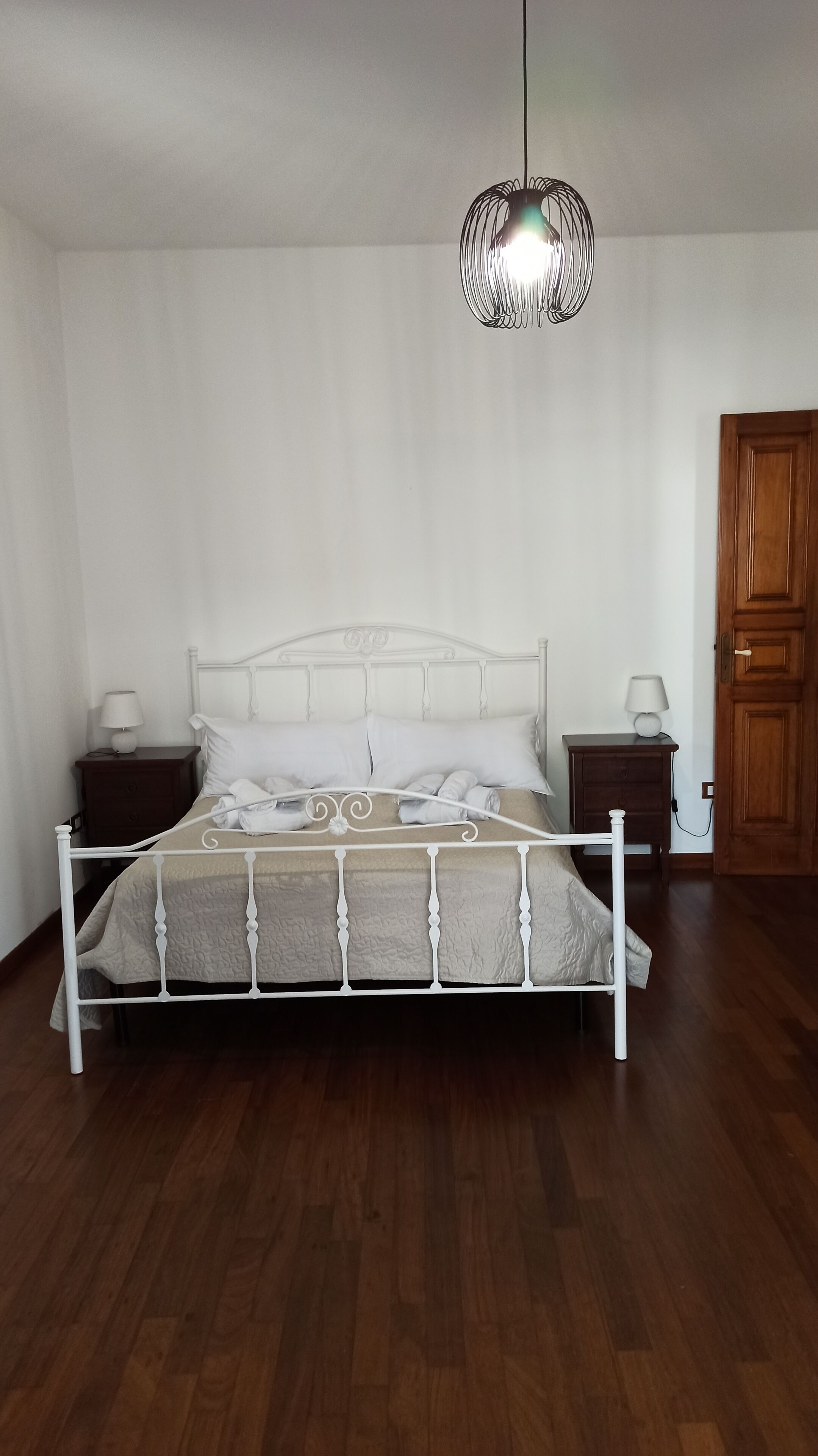 Een slaapkamer met een bed met wit metalen frame, een houten deur en een hanglamp.