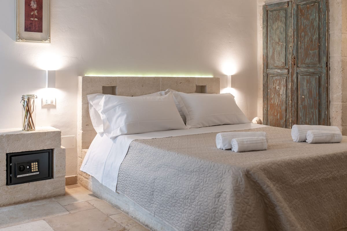A neatly made bed with white linens, a bedside lamp, and a small safe on the nightstand.