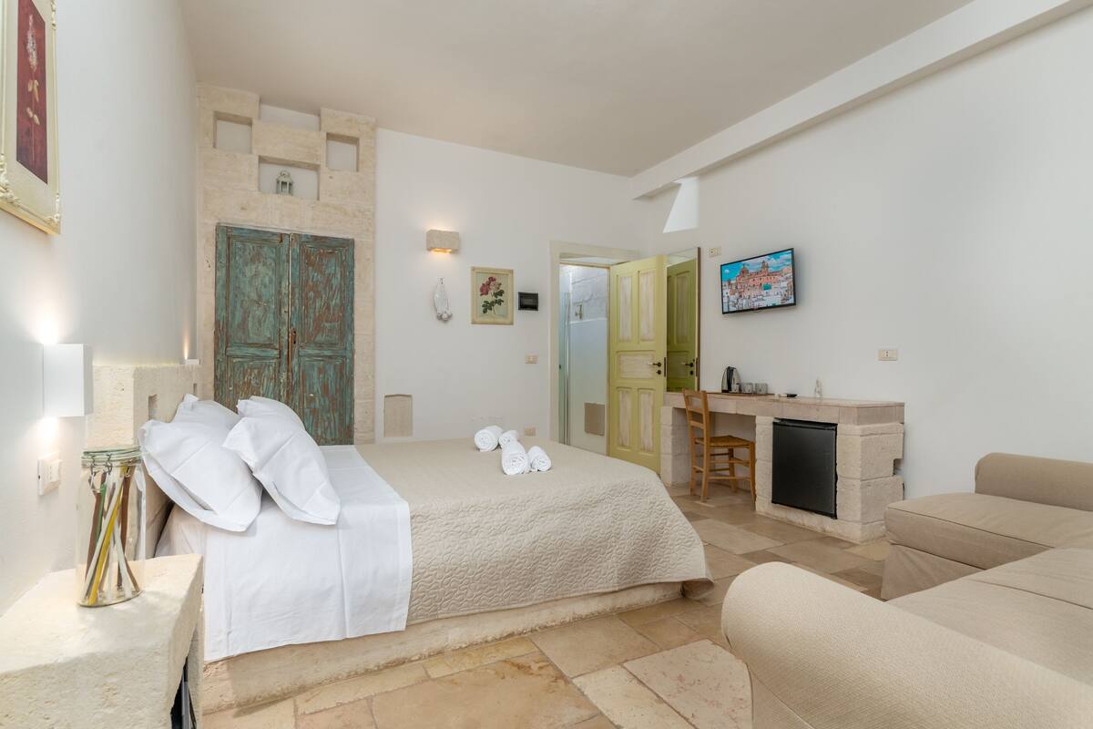 A hotel room with a bed, a desk, a fireplace, and a TV.