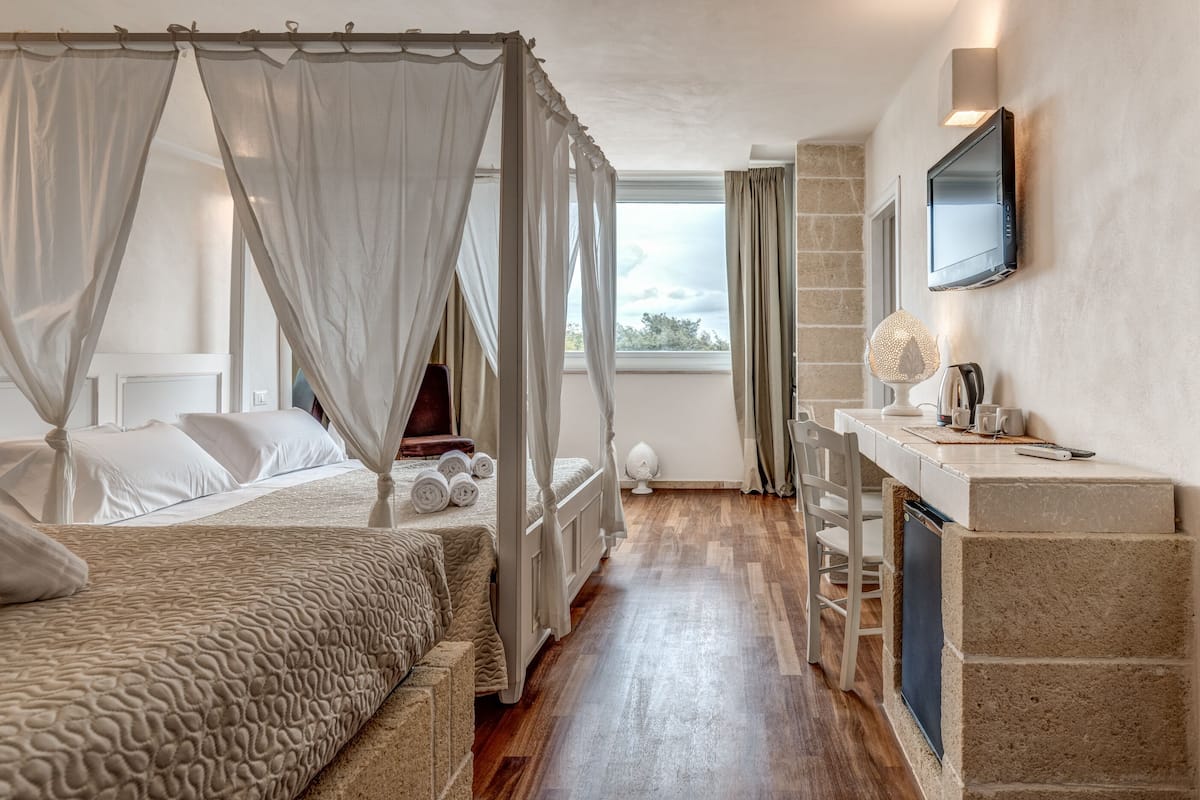 A bedroom with a four-poster bed, a bedside table with a lamp, and a TV mounted on the wall.
