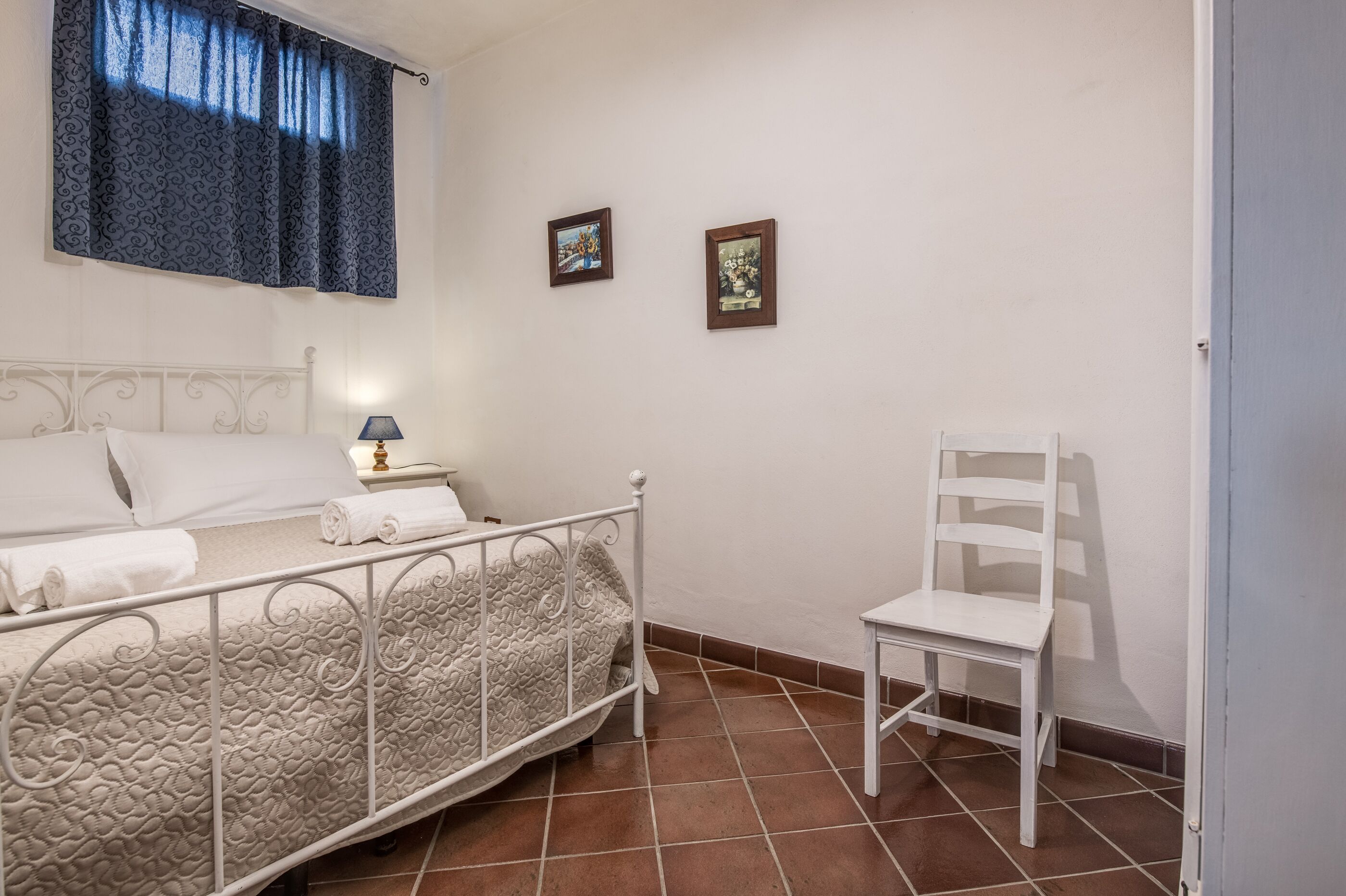 Ein Schlafzimmer mit einem Bett, einem Sessel, einem Nachttisch und zwei gerahmten Bildern an der Wand.