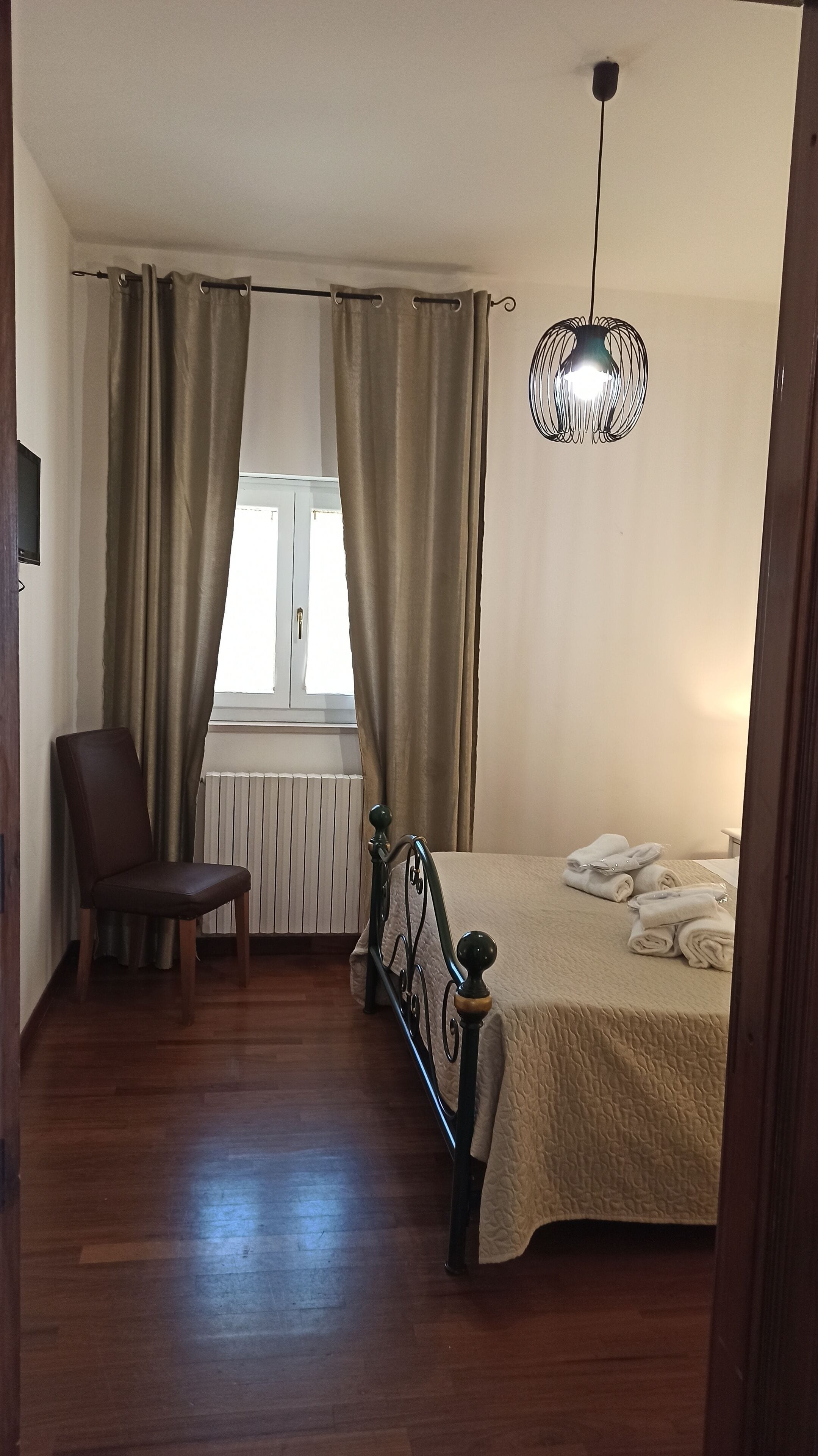 A bedroom with a bed, a chair, a radiator, and a window with curtains.