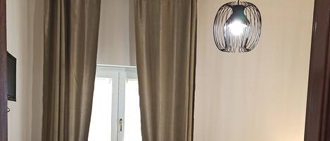 A bedroom with a bed, a chair, a radiator, and a window with curtains.
