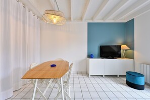 A modern room with a wooden table, white chairs, a TV on a white cabinet, and a blue accent wall. - LES SAULES - 750m plage - Parking (Pornichet)
