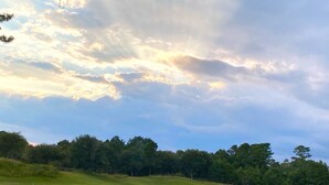 Un parcours de golf avec un étang, des arbres et un ciel nuageux.