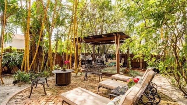 Een terras met loungestoelen, een barbecue en een pergola, omgeven door weelderige beplanting.
