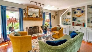 Een woonkamer met een open haard, gele fauteuils, een groene bank en een boekenkast.