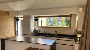 Una cocina moderna con una isla grande, taburetes de madera, un ventanal con vistas y un horno empotrado.