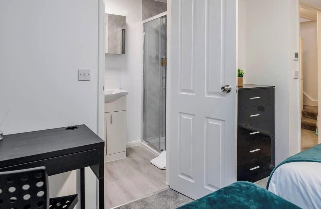 A bedroom with a bed, a desk, a chair, a wardrobe, and a shower area.