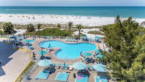 A pool area with lounge chairs and umbrellas, a beach with umbrellas, and a view of the ocean.