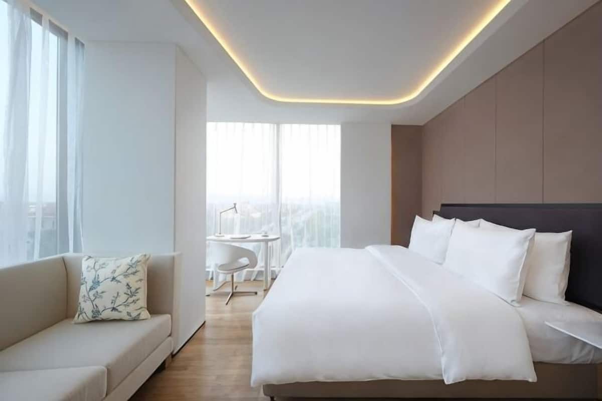 Ein modernes Hotelzimmer mit einem großen Bett, einer Couch, einem Schreibtisch und Blick auf die Stadt.