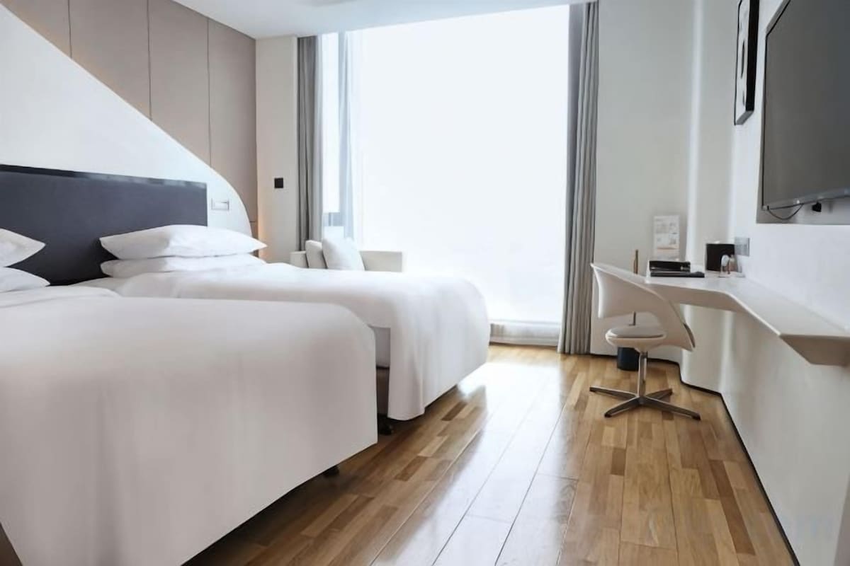Et hotelværelse med to senge, et skrivebord og et stort vindue.