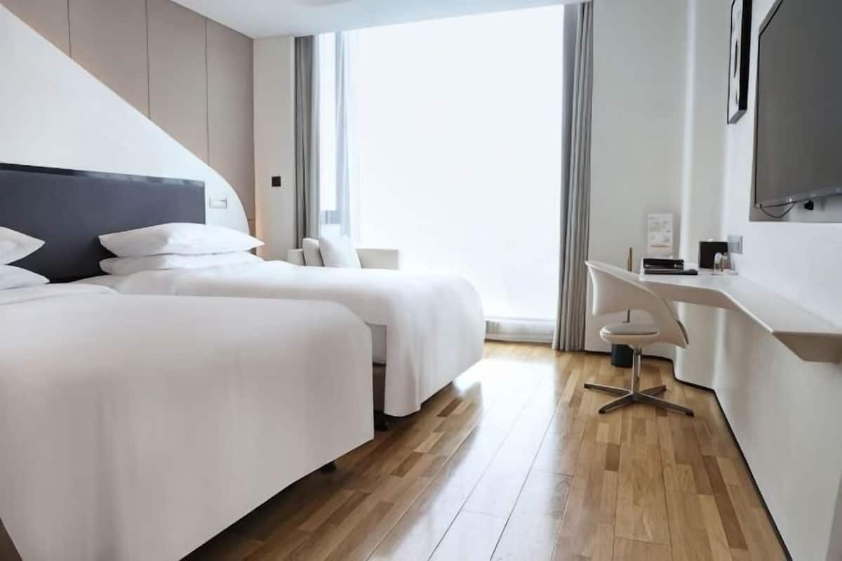 Ein Hotelzimmer mit zwei Betten, einem Schreibtisch, einem Stuhl und einem großen Fenster.
