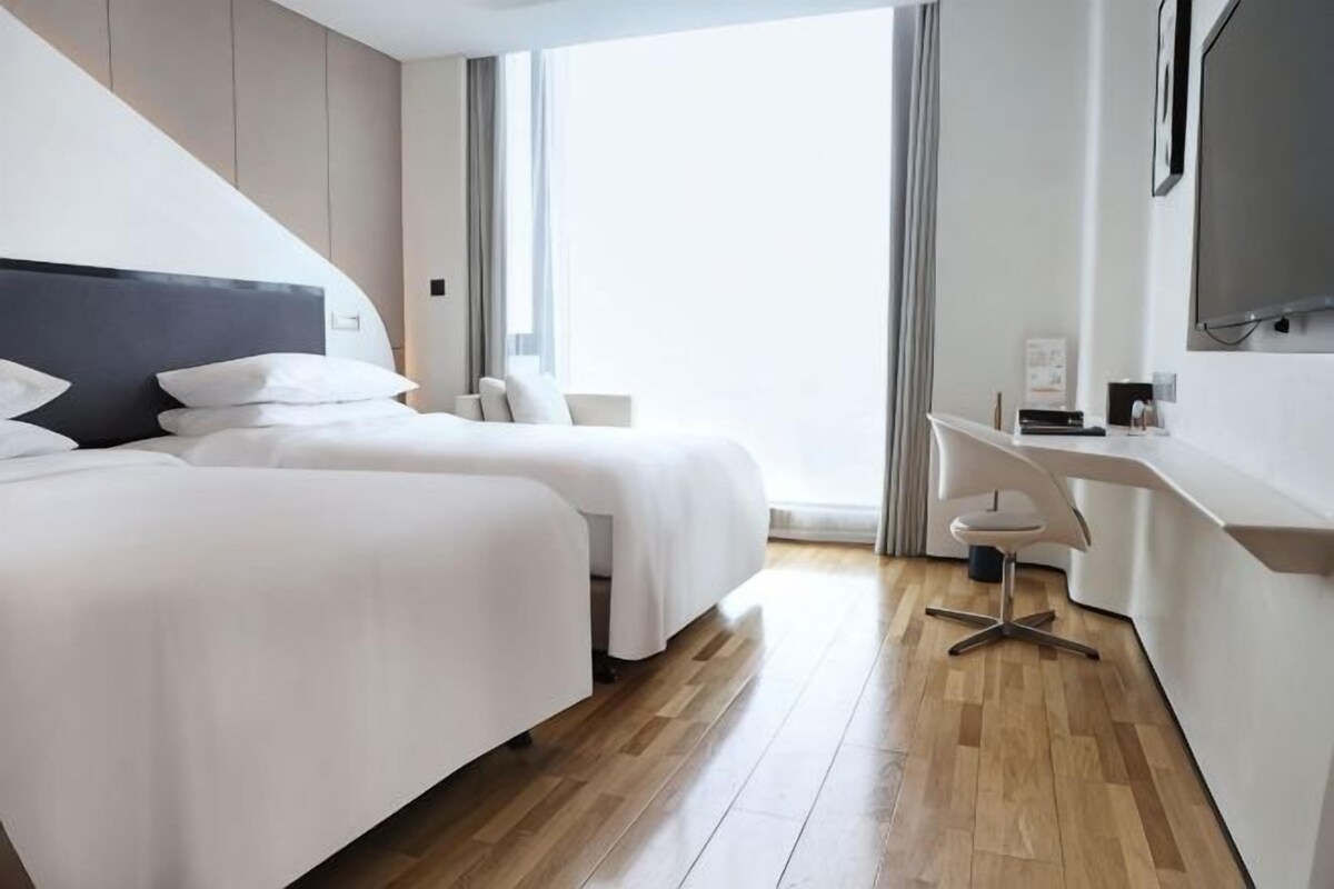 Habitación de hotel con dos camas, un escritorio, una silla y un ventanal grande.