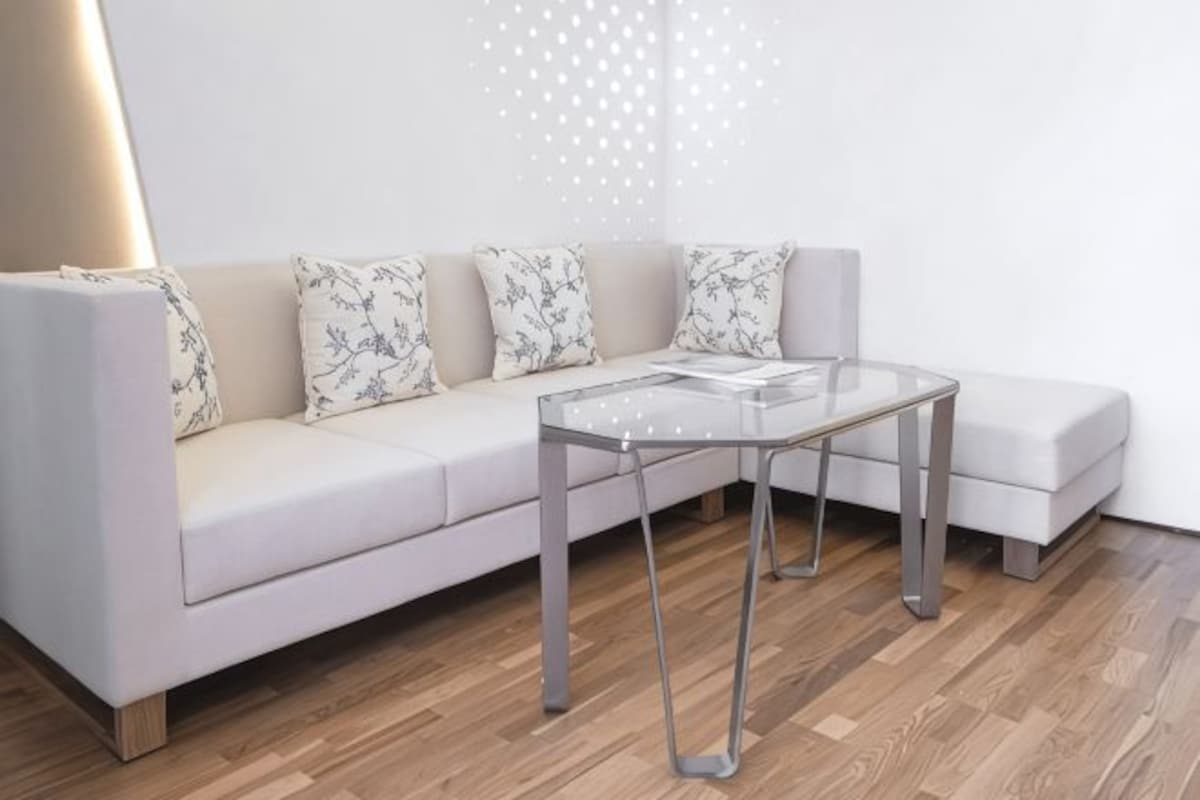 A modern living room with a sofa, a glass coffee table, and a patterned throw pillow.
