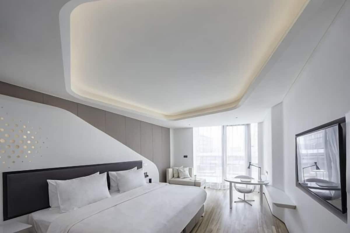 A modern hotel room with a large bed, a desk, and a view of the city.