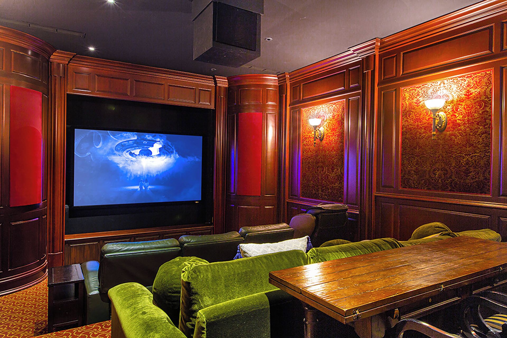 A home theater with a large screen, green velvet seating, and wooden paneling.