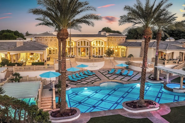 A hotel with a swimming pool, lounge chairs, and palm trees.