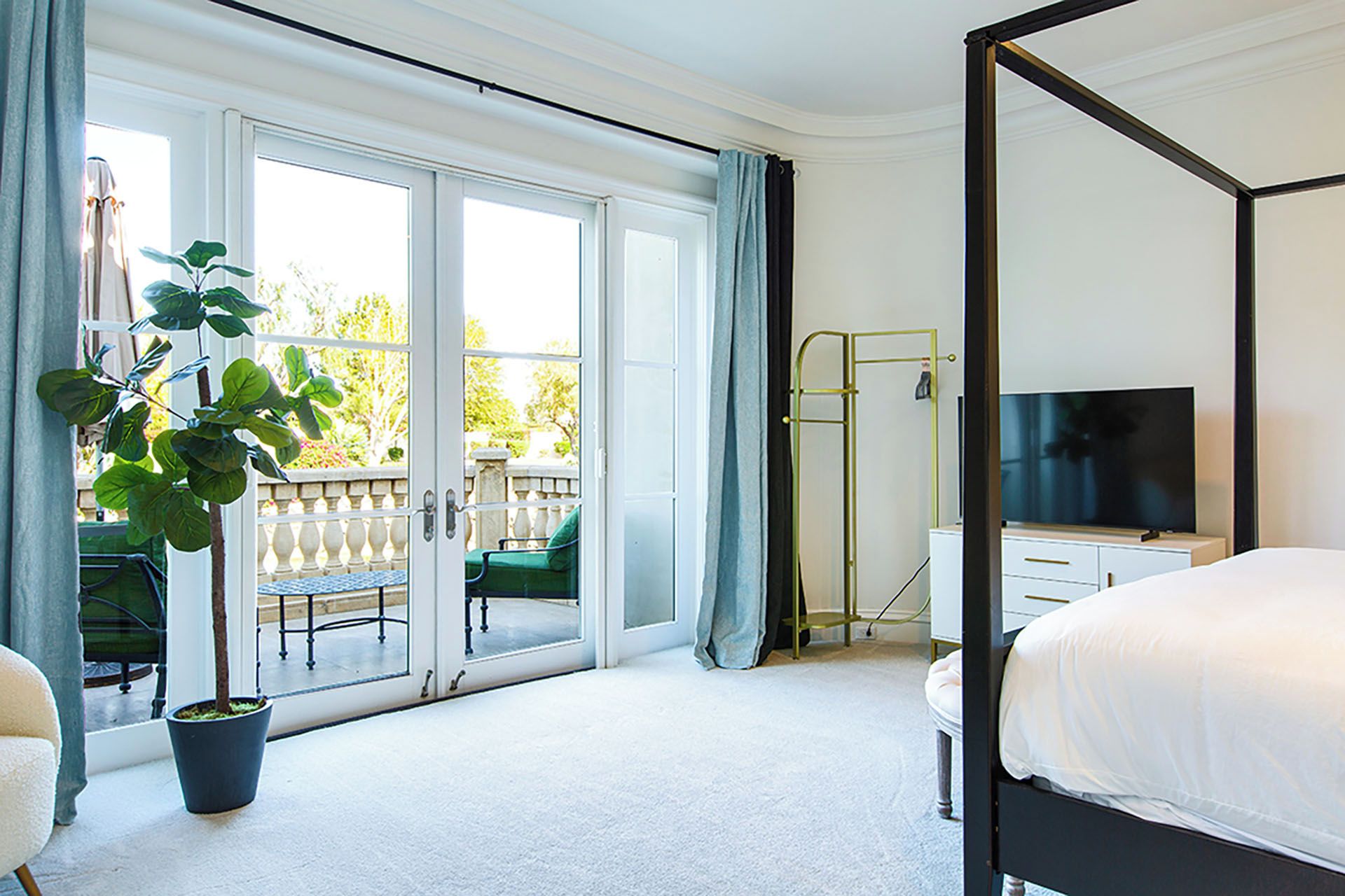 Ein Schlafzimmer mit einem Himmelbett, einem Fernseher, einem Schreibtisch und einem Balkon mit Stuhl und Pflanze.