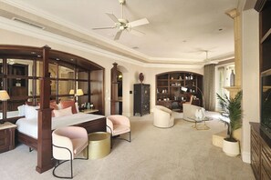 Ein geräumiges Hotelzimmer mit einem großen Bett, einer Sitzecke mit Sofa und Sesseln, einem Esstisch und einem großen Bogenförmigen Spiegel.