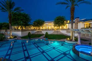 A pool area with a geometric tile pattern, surrounded by palm trees and a well-lit building with a grand entrance.