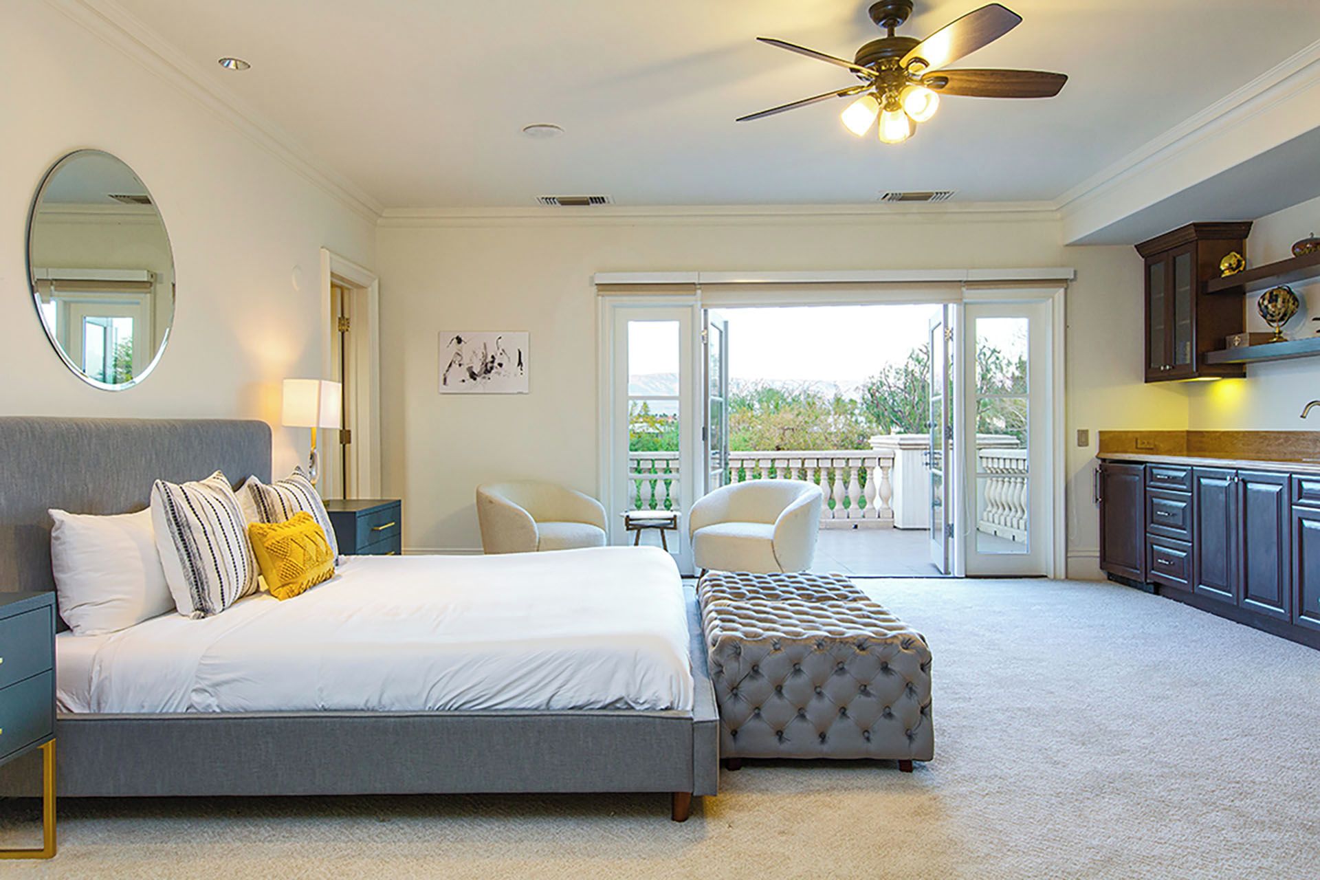 A bedroom with a bed, a seating area, a balcony, and a kitchenette.