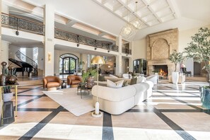 A spacious living area with a grand piano, a fireplace, and a high ceiling with skylights.