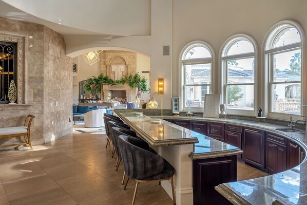 A spacious kitchen with a curved island, dark wooden cabinets, and large windows providing natural light.