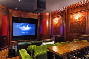A home theater with a large screen, green velvet seating, and wooden paneling.