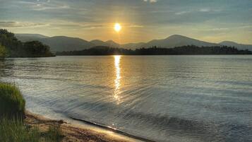 Un lago tranquilo con montañas al fondo y el sol reflejándose en el agua.